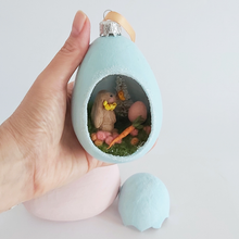 Cargar imagen en el visor de la galería, A vintage style spun cotton Easter bunny diorama ornament being held in a hand against a white background. Pic 2 of 8. 

