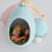 Cargar imagen en el visor de la galería, Another close-up of vintage style spun cotton Easter bunny diorama ornament. It lays against pink and light blue egg ornaments, on a white background. Pic 4 of 8. 
