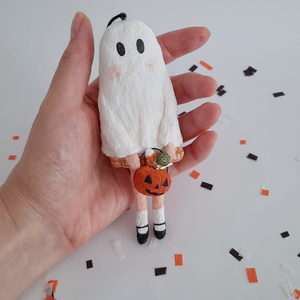 A hand holding a vintage style, spun cotton ghost girl ornament over Halloween confetti on a white background. Pic 2 of 8. 