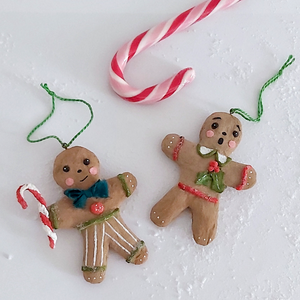 A vintage style spun cotton gingerbread man and gingerbread girl ornaments, laying on a white background. A candy cane lays above them. Pic 8 of 8. 