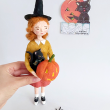 Load image into Gallery viewer, A hand holding a vintage style, spun cotton Halloween girl art doll. A vintage style Halloween greeting hangs in the background. Pic 2 of 7.
