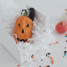 Load image into Gallery viewer, A vintage style spun cotton jack-o-lantern and crow ornament, laying in a white gift box on white shredding. Orange and white spun cotton pumpkins sit behind the box on Halloween confetti. Pic 5 of 8. 
