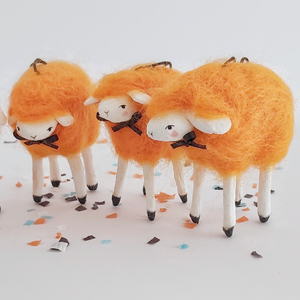 A close view of three, vintage style spun cotton needle felted orange sheep. They stand on Halloween confetti, against a white background. Pic 4 of 5. 