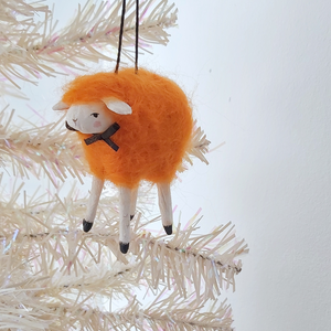 An orange, vintage style spun cotton needle felted sheep ornament hanging on a white tree. Pic 3 of 5. 