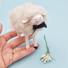Load image into Gallery viewer, A white spun cotton needle felted sheep ornament, held in hand against a light blue background. White flowers sit next to the sheep. Pic 1 of 6. 
