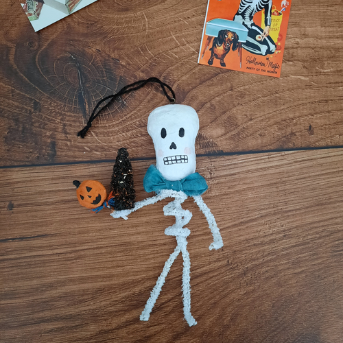 A vintage style, spun cotton pipe cleaner skeleton laying on a wooden background. Pic 1 of 5.