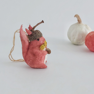 A side view of a vintage style spun cotton red squirrel ornament, next to spun cotton pumpkins on a white background. Pic 6 of 9. 