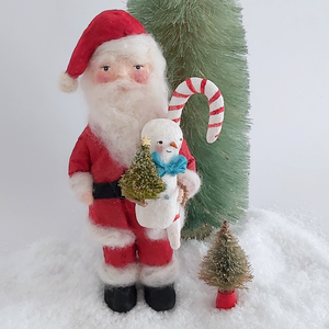 A vintage style spun cotton Santa art doll standing next to bottle brush trees against a white background. Pic 1 of 9. 