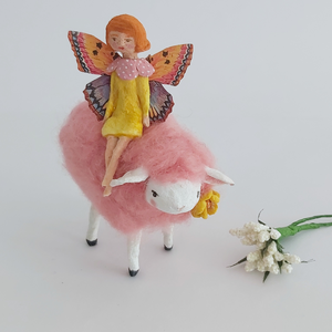 A vintage style spun cotton fairy sitting on a pink sheep. Decorative white flowers lay next to them on a white background. Pic 4 of 7. 