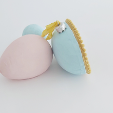 Load image into Gallery viewer, A side view of a vintage style spun cotton sheep diorama egg ornament. It&#39;s laying against pink and light blue egg ornaments. Pic 5 of 6. 
