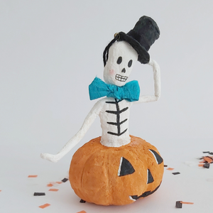 A closer view of a vintage style, spun cotton skeleton in a jack-o-lantern. It's sitting on Halloween confetti against a white background. Pic 4 of 7. 