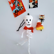 Load image into Gallery viewer, A vintage style, spun cotton pipe cleaner skeleton laying next to vintage skeleton Halloween illustrations. Pic 1 of 4.
