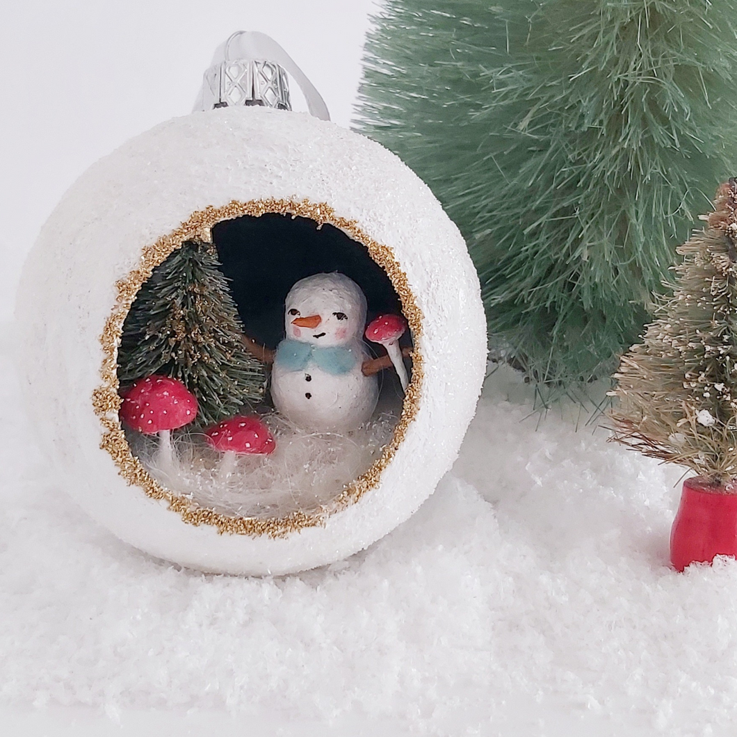 A vintage style spun cotton snowman diorama ornament sitting next to two bottle brush trees. Pic 1 of 6. 