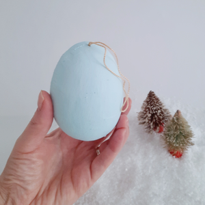 A back view of a vintage style, spun cotton snowman diorama ornament held in a hand against a white background. Pic 6 of 6. 
