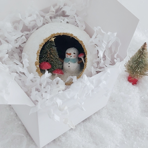 A vintage style spun cotton snowman diorama ornament, laying in a white gift box next to a mini bottle brush tree. Pic 5 of 6. 