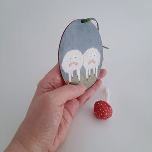 An image of a hand holding a wooden sheep ornament . A spun cotton red mushroom sits nearby. Pic 3 of 6. 