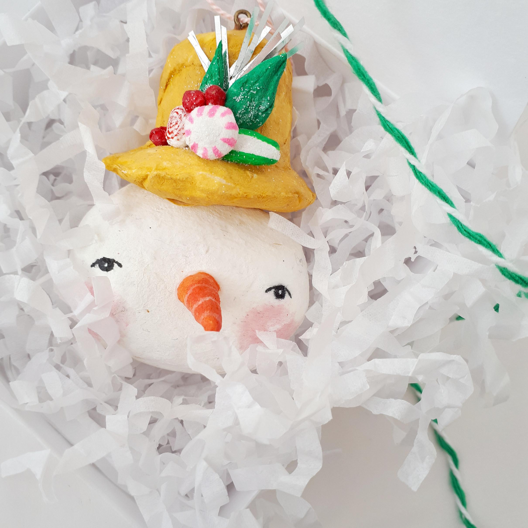 Spun cotton snowman laying in a white box with white tissue shreds and green bakers twine. Photo 5