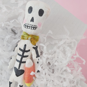 Spun cotton skeleton sculpture, laying in white gift box with white tissue shreds. 