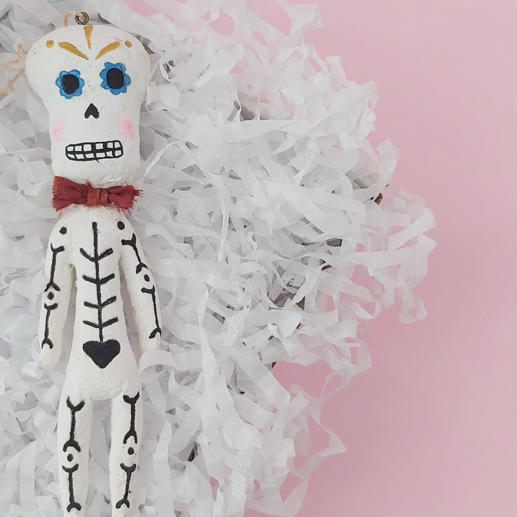 Spun cotton Dia de los Muertos skeleton ornament, laying in box. Photo 1