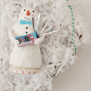 Snowman lying in box with white shredded paper and bakers twine. Photo 7 of 7.