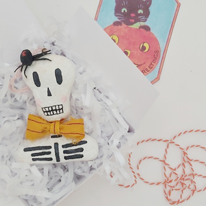 Spun cotton skeleton bust ornament, laying in gift box with shredded tissue paper. Pic 4 of 5.