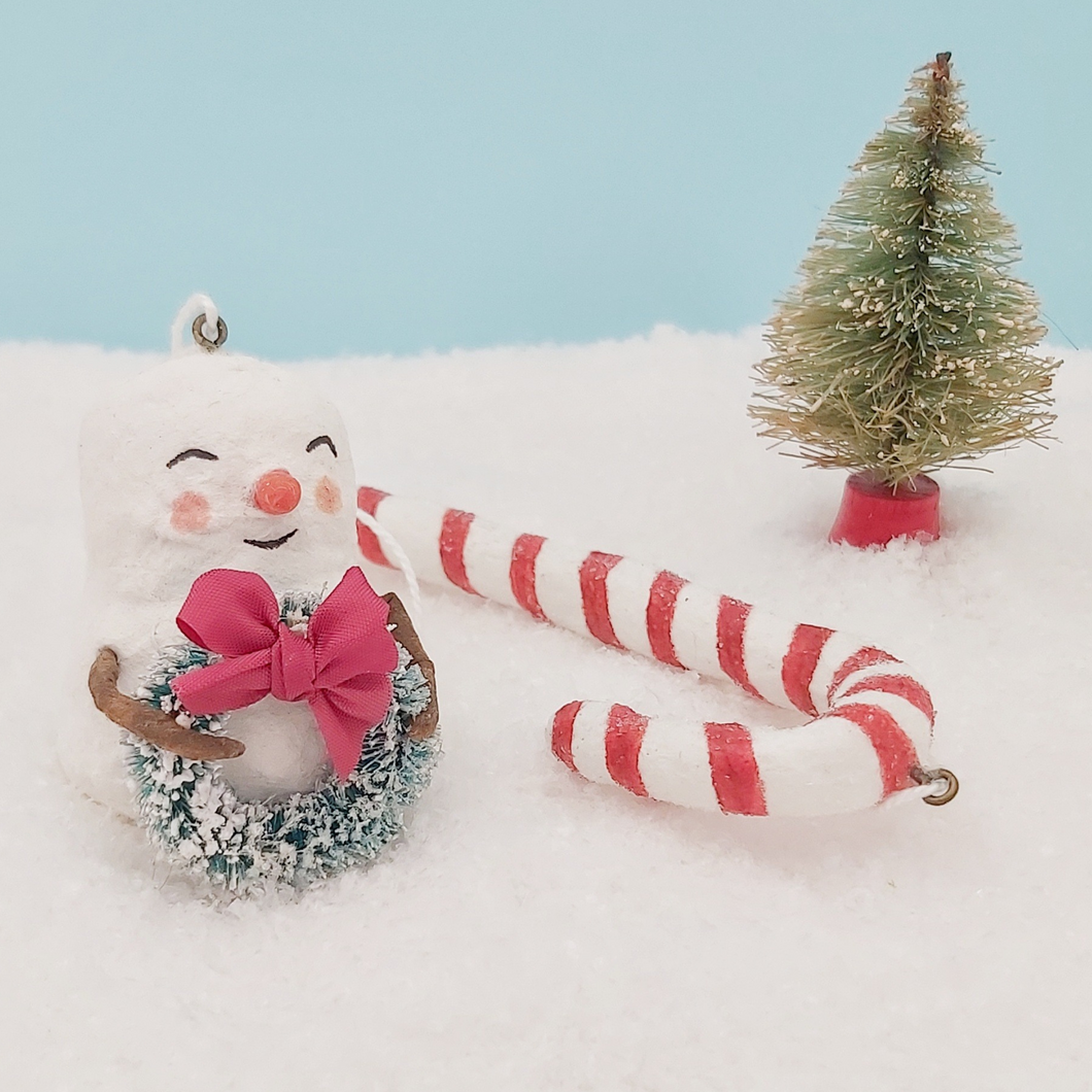 Spun cotton snowman holding bottlebrush wreath and sitting next to spun cotton candy cane. Pic 1 of 7.