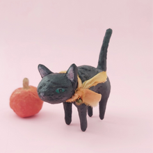 Cargar imagen en el visor de la galería, Black spun cotton cat sculpture, wearing an orange bow made from silk sari scraps, and a jingle bell. 
