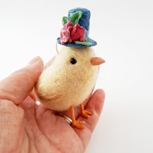 Yellow needle felted chick wearing blue spun cotton top hat with flowers, side view, sitting in a hand (picture 3)