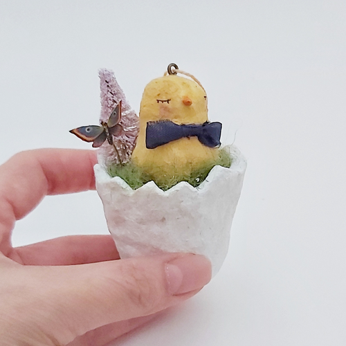 Vintage style spun cotton chick sitting in a cracked egg, held by hand against a white background. Pic 2 of 6.