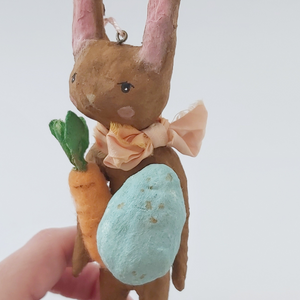 Close up of spun cotton chocolate brown bunny, holding light blue egg and felted carrot. Pic 2 of 8.