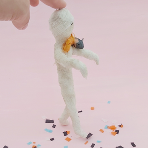 Opposite side view of spun cotton mummy and mouse ornament, standing on Halloween confetti while being supported by hand. Pic 8 of 8. 