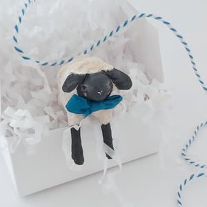 A miniature spun cotton sheep hanging out of a white gift box in white tissue shredding against a white background. Pic 4 of 8. 