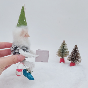 Side view of vintage style spun cotton pine cone elf sitting on a spun cotton candy cane. Pic 5 of 10. 