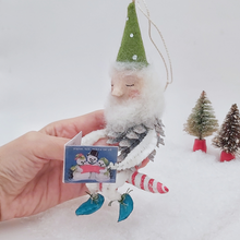 Load image into Gallery viewer, Vintage style spun cotton pine cone elf sitting on a spun cotton candy cane. He&#39;s held in hand against a white background with vintage bottle brush trees in the distance. Pic 1 of 10. 
