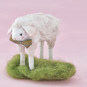 A vintage style spun cotton sheep standing on green wool grass, against a pink background. Pic 1 of 8.