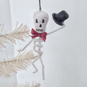 Image of a vintage style spun cotton skeleton ornament hanging from a white tree. Pic 2 of 6.