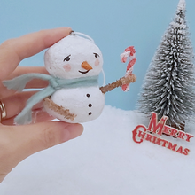 Load image into Gallery viewer, Vintage style spun cotton snowman, held in hand for size comparison. He&#39;s against a light blue background with a bottle brush tree and Merry Christmas sign in the distance. Pic 1 of 7.
