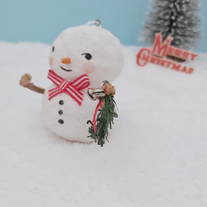 Close up of garland and silver jingle bells that the spun cotton snowman is holding. He's sitting on fake snow against a light blue background with a bottle brush tree and vintage Merry Christmas decoration in the distance. Pic 4 of 7.