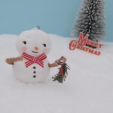 Load image into Gallery viewer, Vintage style spun cotton snowman holding garland. He&#39;s standing on fake snow against a light blue background with a bottle brush tree and Merry Christmas sign in the distance. Pic 2 of 7.

