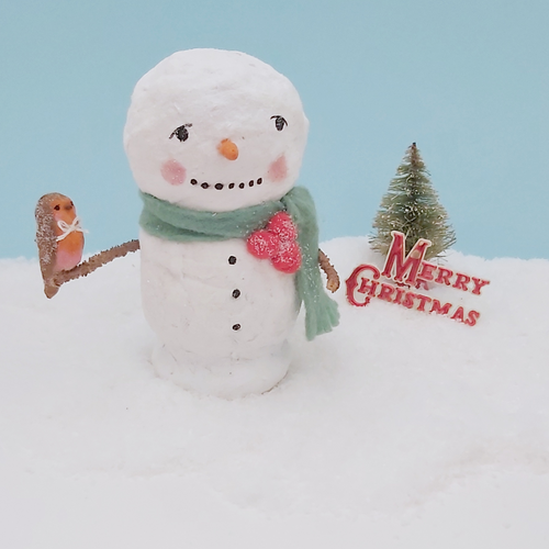 Vintage style spun cotton snowman holding a spun cotton robin on his arm. He sits on snow, against a light blue background and in front of a vintage bottle brush tree and Merry Christmas sign. Pic 1 of 7.