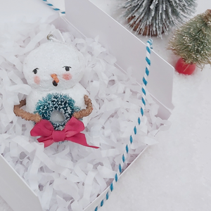 Vintage style spun cotton snowman laying in white gift box, next to bottle brush trees on a white background. Pic 5 of 8.