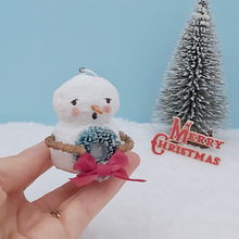 Load image into Gallery viewer, Vintage style spun cotton snowman ornament, held in hand against a light blue background with a bottle brush tree and Merry Christmas decoration in the distance. Pic  2 of 8.

