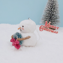 Load image into Gallery viewer, Opposite side view of vintage style spun cotton snowman. He&#39;s against a light blue background, sitting on snow, with a bottle brush tree in the distance. Pic  7 of 8.
