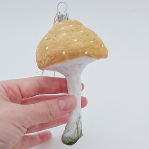 A hand holding a vintage style spun cotton yellow mushroom ornament, against a white background. Pic 1 of 4.